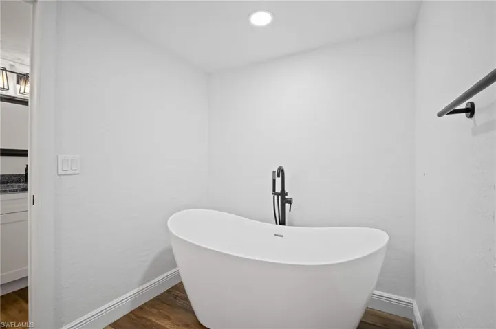 Full bathroom featuring dark wood-type flooring, a freestanding bath, vanity, and a textured wall