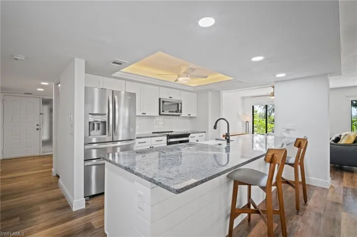 Kitchen featuring a tray ceiling, light stone counters, stainless steel appliances, white cabinetry, and recessed lighting