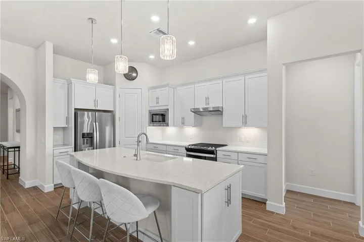 Kitchen featuring a kitchen bar, arched walkways, white cabinetry, wood finish floors, and recessed lighting