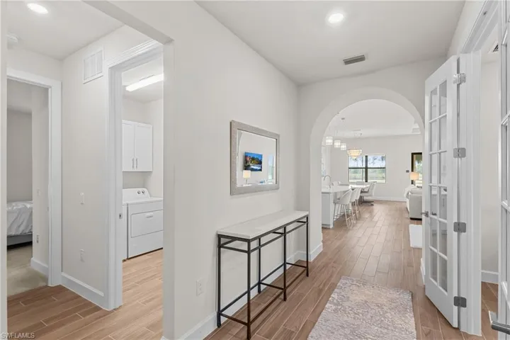 Corridor with wood finish floors, arched walkways, washer / clothes dryer, and recessed lighting