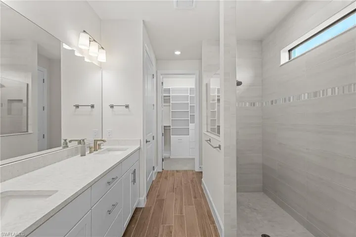 Full bath with walk in shower, double vanity, a spacious closet, wood finish floors, and recessed lighting