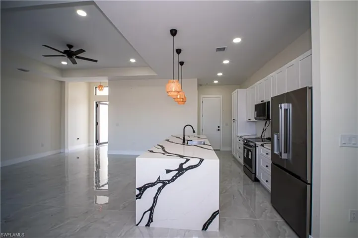 Kitchen featuring stainless steel appliances, white cabinetry, decorative light fixtures, a ceiling fan, and a tray ceiling