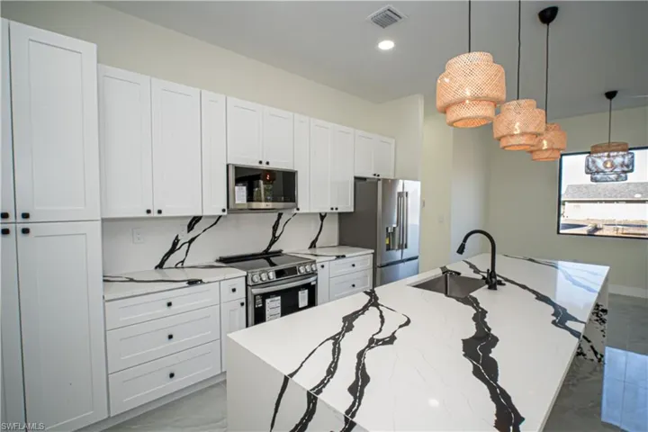 Kitchen featuring a kitchen island with sink, hanging light fixtures, white cabinetry, stainless steel appliances, and light stone counters