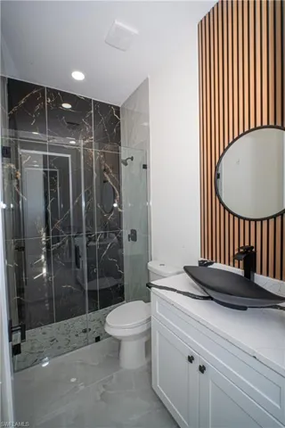 Full bath with vanity, a marble finish shower, recessed lighting, and light marble finish floors