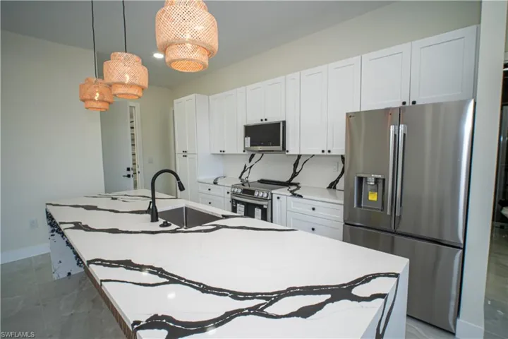 Kitchen with stainless steel appliances, pendant lighting, white cabinetry, an island with sink, and light stone countertops