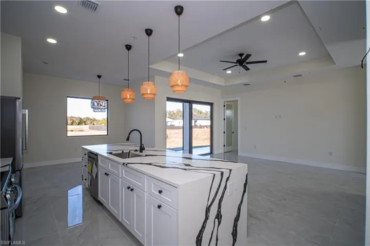 Kitchen featuring pendant lighting, light stone countertops, open floor plan, stainless steel appliances, and a tray ceiling