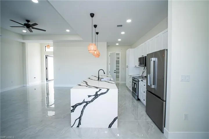 Kitchen featuring white cabinets, stainless steel appliances, decorative light fixtures, a ceiling fan, and light stone countertops