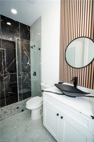 Bathroom featuring vanity, a marble finish shower, and light marble finish floors