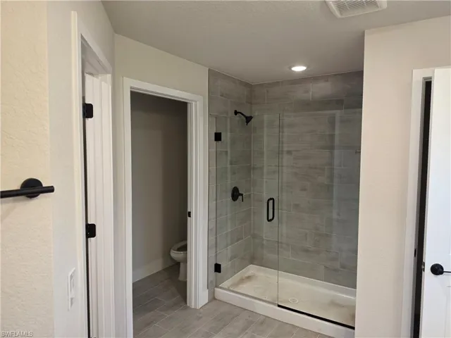 Spacious bathroom featuring a glass-enclosed shower with tile surround and black fixtures, integrated ceiling lighting, and a separate water closet