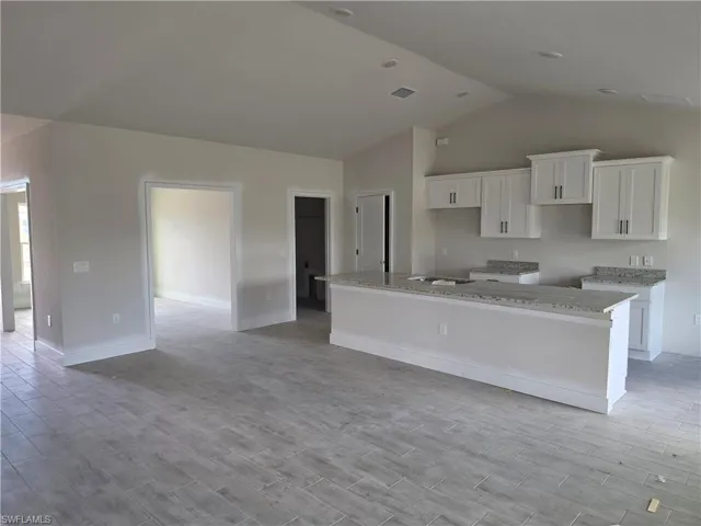 The open concept kitchen and living area features white cabinetry, granite countertops, and light-toned tile flooring