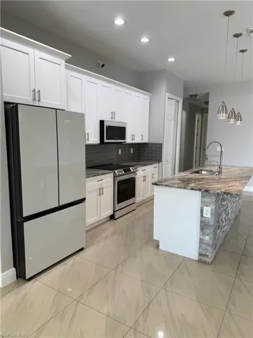 Kitchen featuring stainless steel appliances, dark stone counters, white cabinets, and a center island with sink