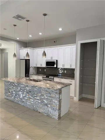 Kitchen featuring light stone counters, white cabinets, pendant lighting, and stainless steel appliances