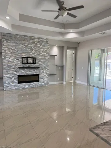 Unfurnished living room featuring a raised ceiling, a ceiling fan, a stone fireplace, and recessed lighting