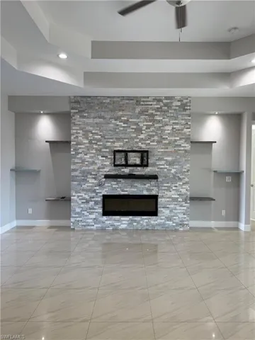 Unfurnished living room with a glass covered fireplace, ceiling fan, recessed lighting, and a raised ceiling