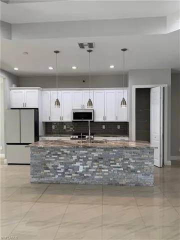Kitchen featuring white cabinets, freestanding refrigerator, and pendant lighting