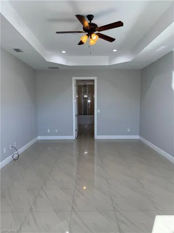 Empty room with a ceiling fan, a raised ceiling, recessed lighting, and light marble finish flooring