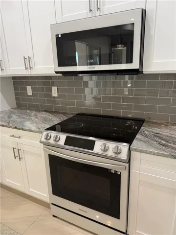 Kitchen with stainless steel appliances, light stone counters, white cabinetry, and decorative backsplash