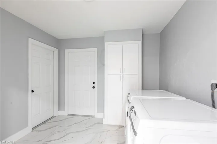 Washroom featuring washing machine and dryer, baseboards, cabinet space, and marble finish floor