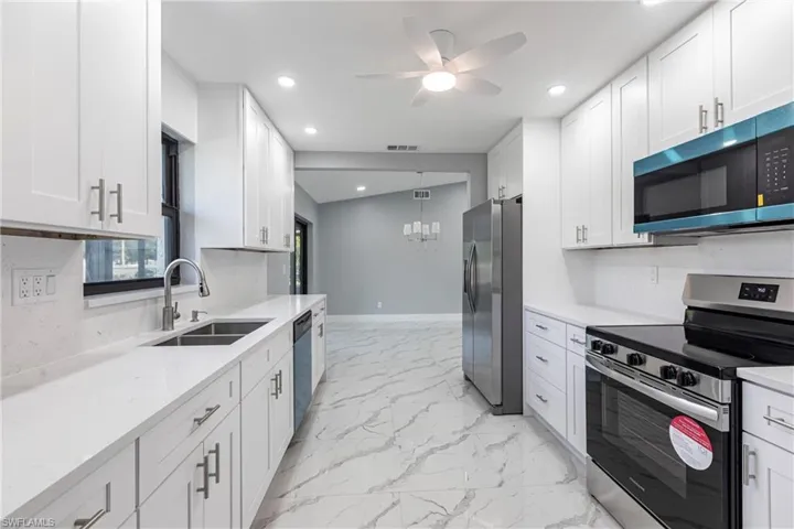 Kitchen with marble finish floor, visible vents, a sink, appliances with stainless steel finishes, and ceiling fan with notable chandelier
