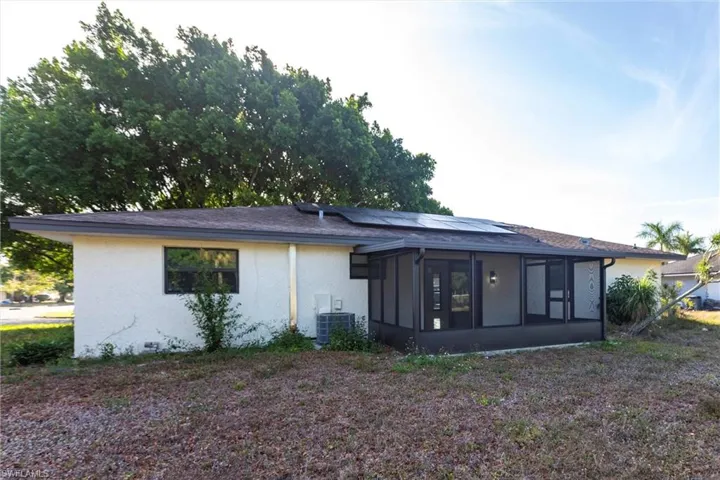 Back of house with solar panels, a sunroom, central air condition unit, and stucco siding