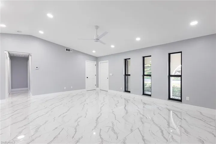 Empty room with vaulted ceiling, visible vents, marble finish floor, and ceiling fan