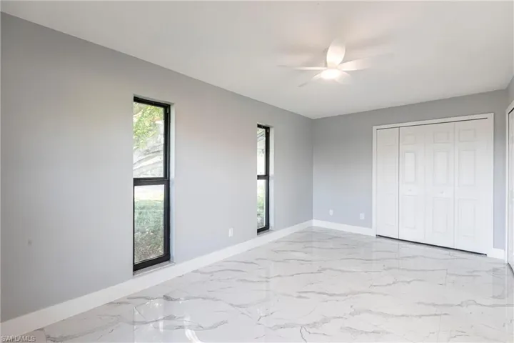 Unfurnished bedroom with marble finish floor, baseboards, and multiple windows