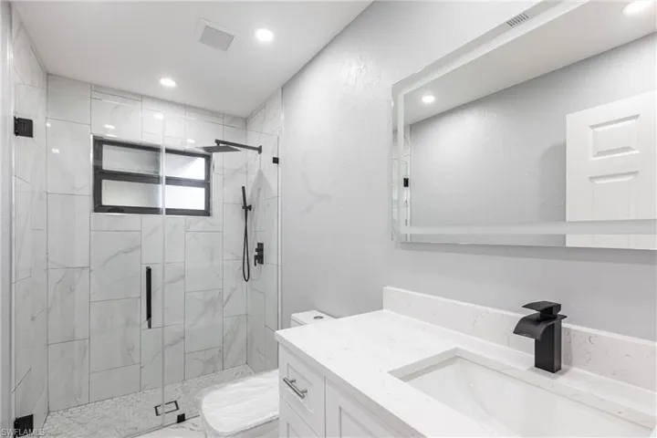 Bathroom featuring a marble finish shower, toilet, visible vents, recessed lighting, and vanity
