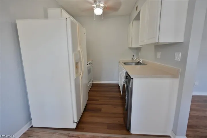 Kitchen with white appliances, white cabinetry, dark wood finished floors, and light countertops