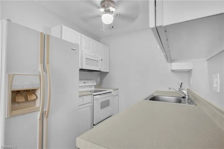 Kitchen with white appliances, white cabinets, light countertops, and a ceiling fan
