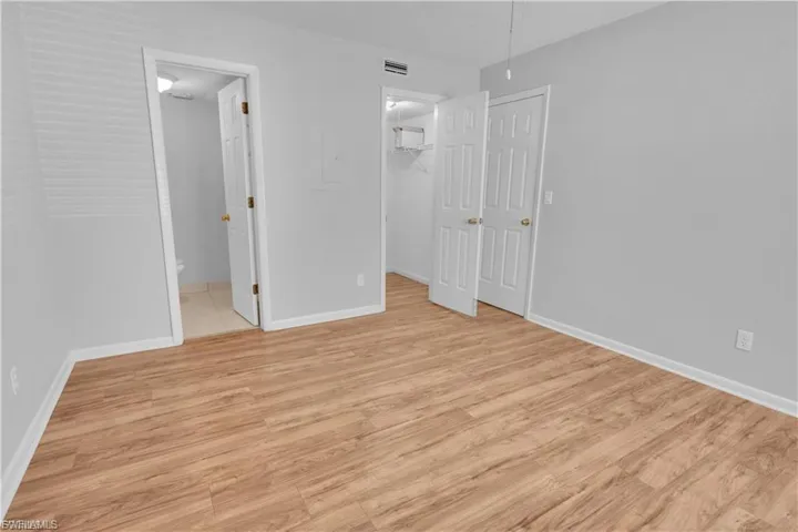 Unfurnished bedroom with a walk in closet, light wood-type flooring, electric panel, and connected bathroom