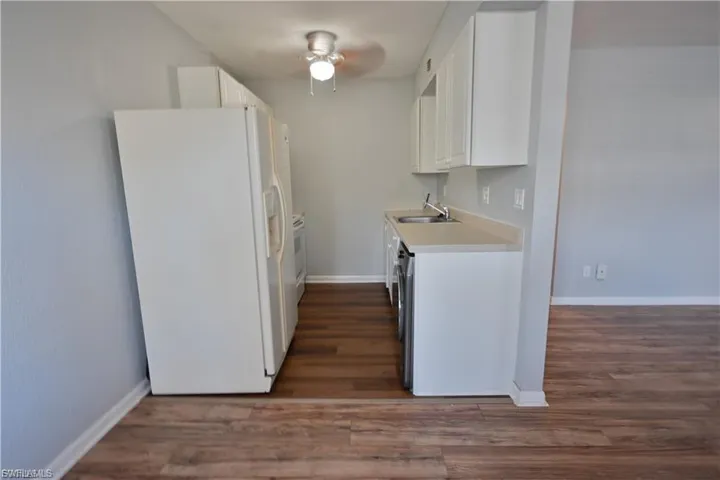 Kitchen featuring white appliances, light countertops, white cabinets, and dark wood-style floors