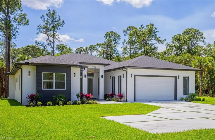 Prairie-style house featuring a front yard, driveway, a garage, stucco siding, and roof with shingles