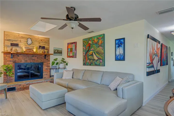 Living area featuring wood finished floors, a skylight, a brick fireplace, and ceiling fan
