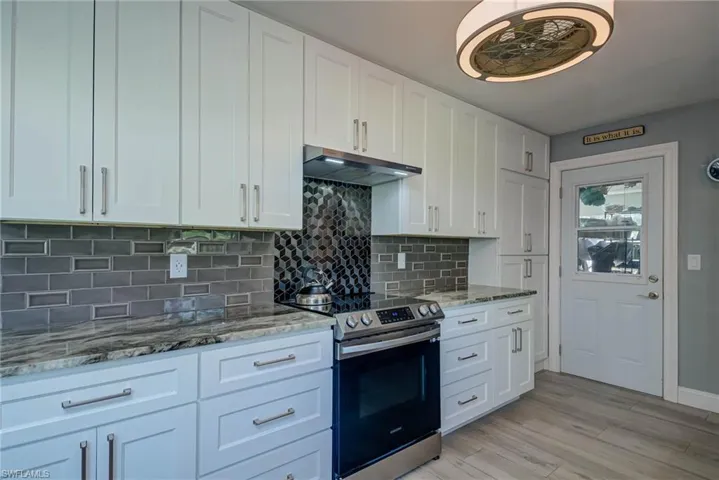 Kitchen with electric stove, white cabinetry, under cabinet range hood, and tasteful backsplash
