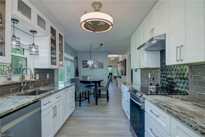 Kitchen featuring tasteful backsplash, range with electric cooktop, white cabinets, and hanging light fixtures
