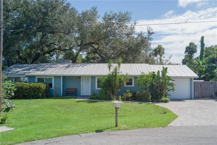 Ranch-style home with a front yard, a metal roof, decorative driveway, and an attached garage