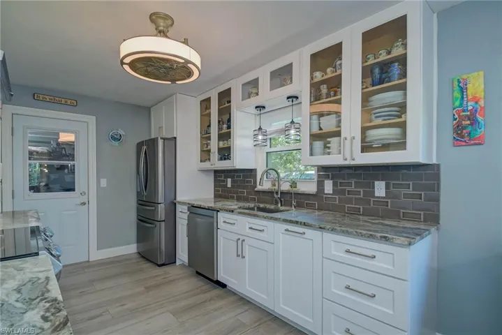 Kitchen with white cabinets, dark stone counters, appliances with stainless steel finishes, decorative light fixtures, and glass insert cabinets