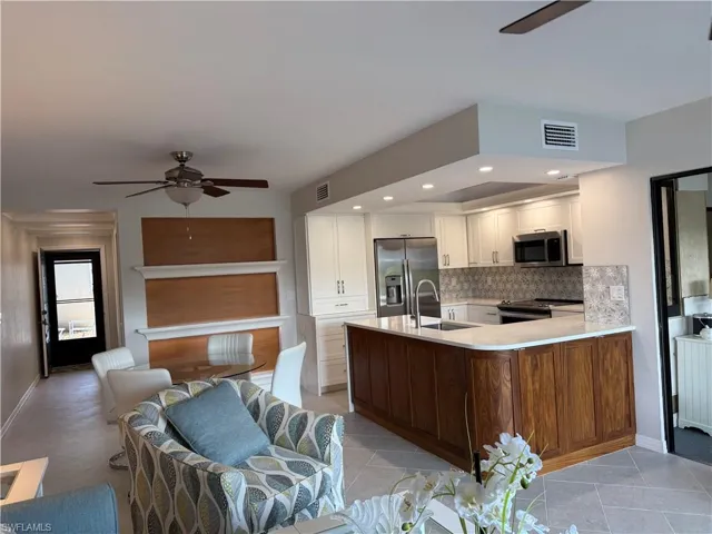 Kitchen featuring a ceiling fan, stainless steel appliances, open floor plan, light stone countertops, and a peninsula