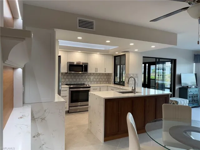 Kitchen featuring light stone countertops, a peninsula, stainless steel appliances, recessed lighting, and white cabinetry