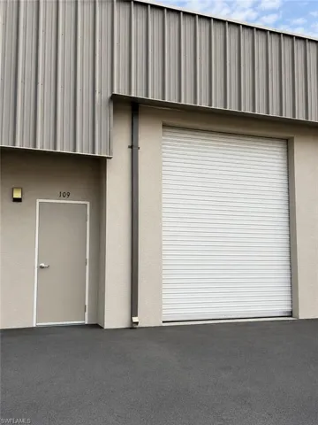 Commercial exterior featuring a large roll-up door, stucco finish, and a corrugated metal upper facade