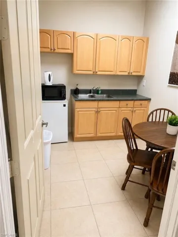 Kitchenette featuring light wood cabinetry, a stainless steel sink, and a dark stone-finish countertop