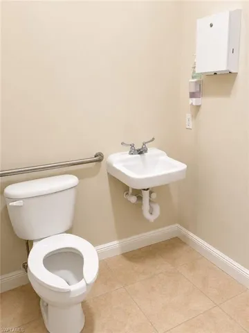 Restroom featuring a wall-mounted sink, toilet with a grab bar, and neutral-toned tile flooring