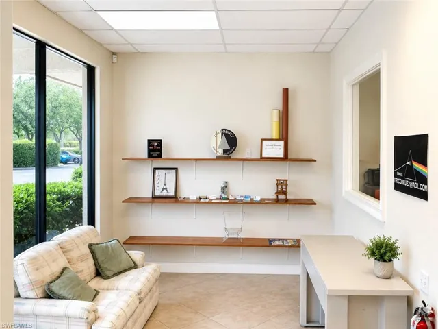Bright interior space featuring a large window, three floating wood-finish shelves, a dropped ceiling with recessed lighting, and tile flooring