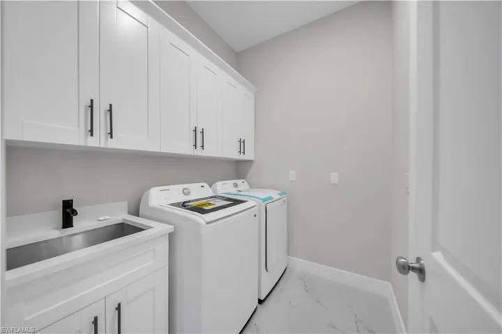 Laundry room with light marble finish floors, cabinet space, and washer and clothes dryer
