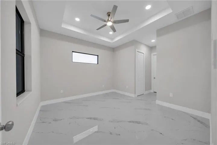 Empty room with recessed lighting, a ceiling fan, a tray ceiling, and light marble finish flooring