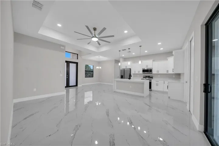 Unfurnished living room featuring recessed lighting, ceiling fan, a chandelier, and a raised ceiling