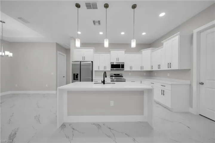 Kitchen featuring appliances with stainless steel finishes, light stone counters, hanging light fixtures, a center island with sink, and white cabinetry