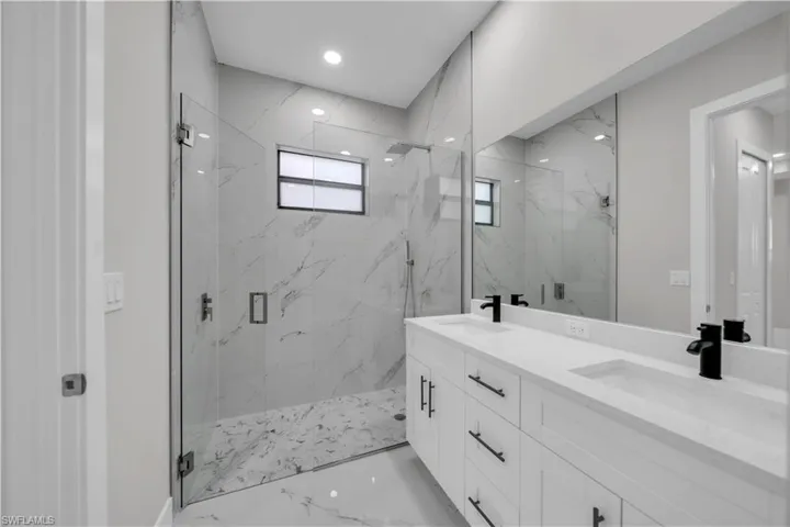 Full bath with a marble finish shower, double vanity, and recessed lighting