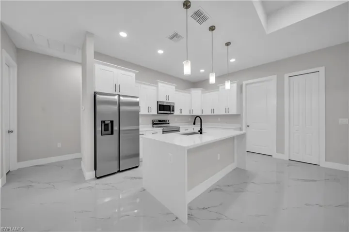 Kitchen with stainless steel appliances, decorative light fixtures, an island with sink, white cabinets, and light stone countertops