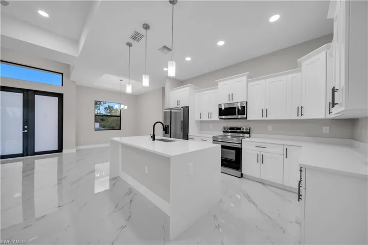 Kitchen with stainless steel appliances, an island with sink, pendant lighting, light stone counters, and white cabinets